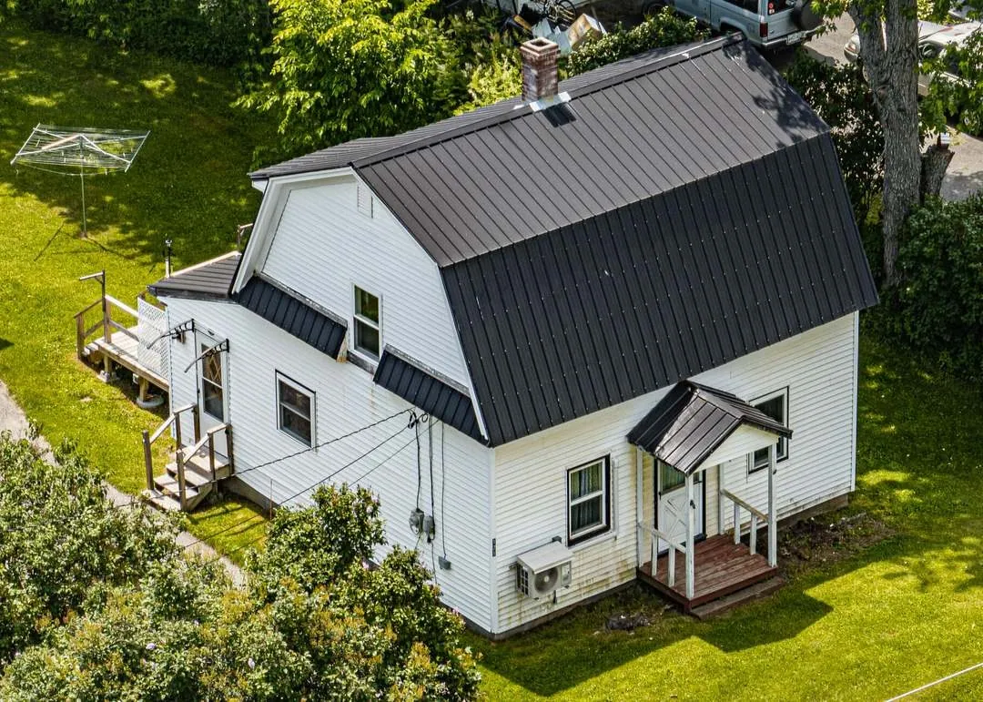 Gambrel-roof farmhouse with metal roof and heat pump in Maine